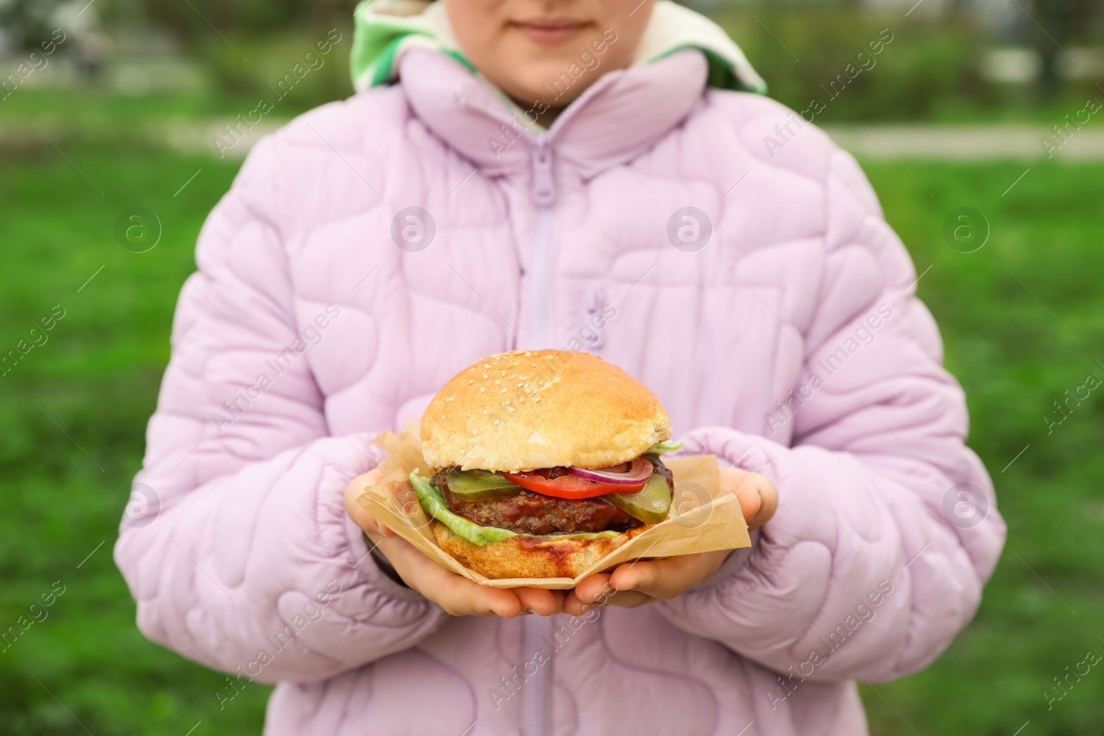 Photo of Little girl holding fresh delicious burger outdoors, closeup. Street food