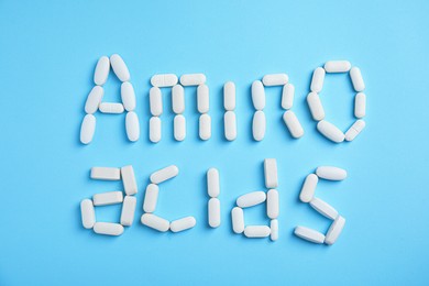Photo of Words "AMINO ACIDS" made with pills on light blue background, flat lay