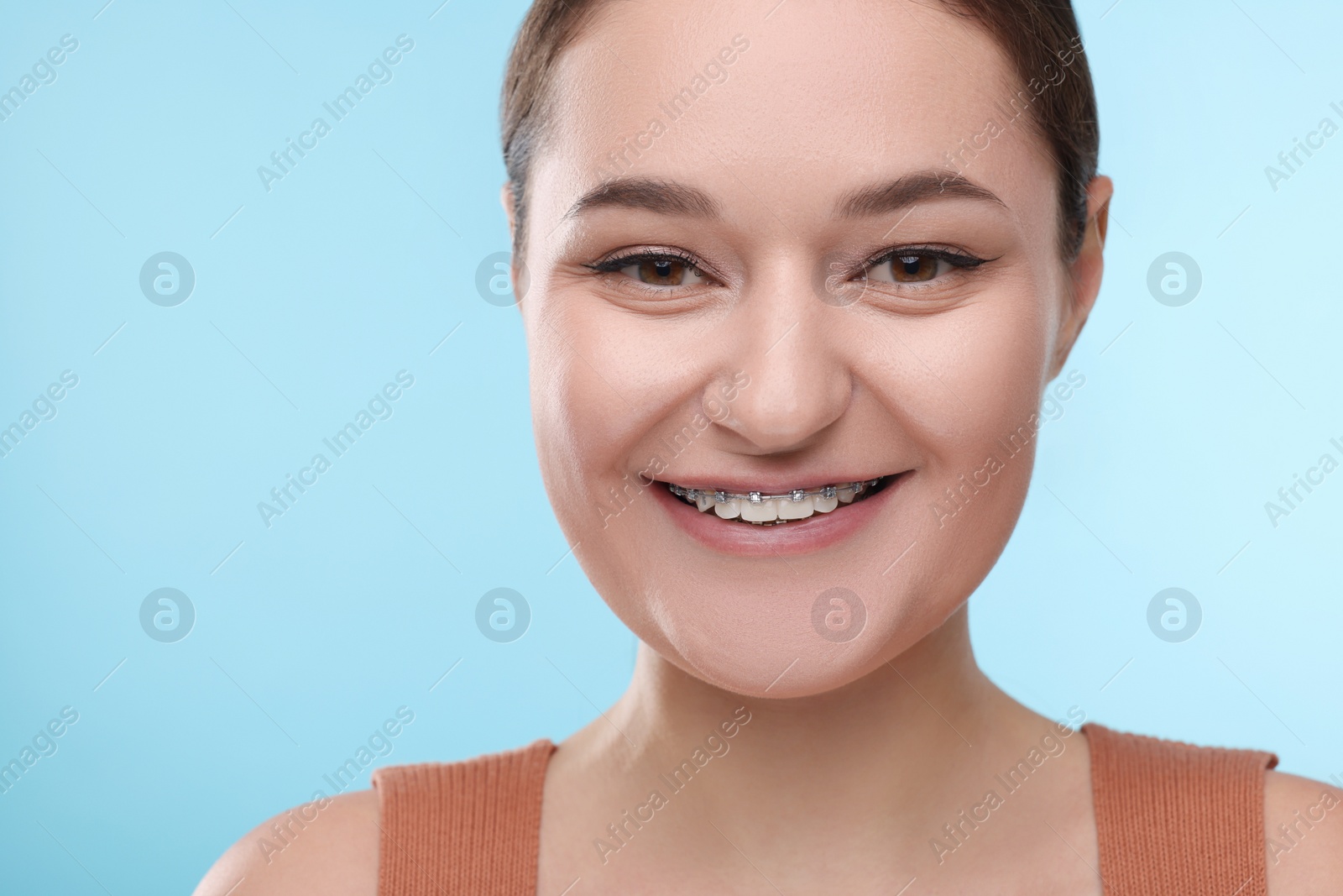 Photo of Smiling woman with dental braces on light blue background, closeup. Space for text