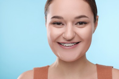 Smiling woman with dental braces on light blue background, closeup. Space for text