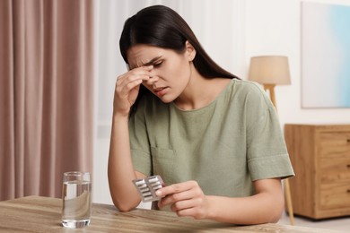 Photo of Sad woman with blister of pills suffering from headache at wooden table indoors