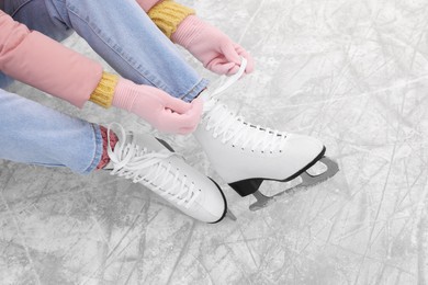 Woman lacing figure skates on ice, above view