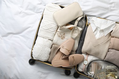 Photo of Open suitcase with folded clothes, shoes and accessories on bed, top view