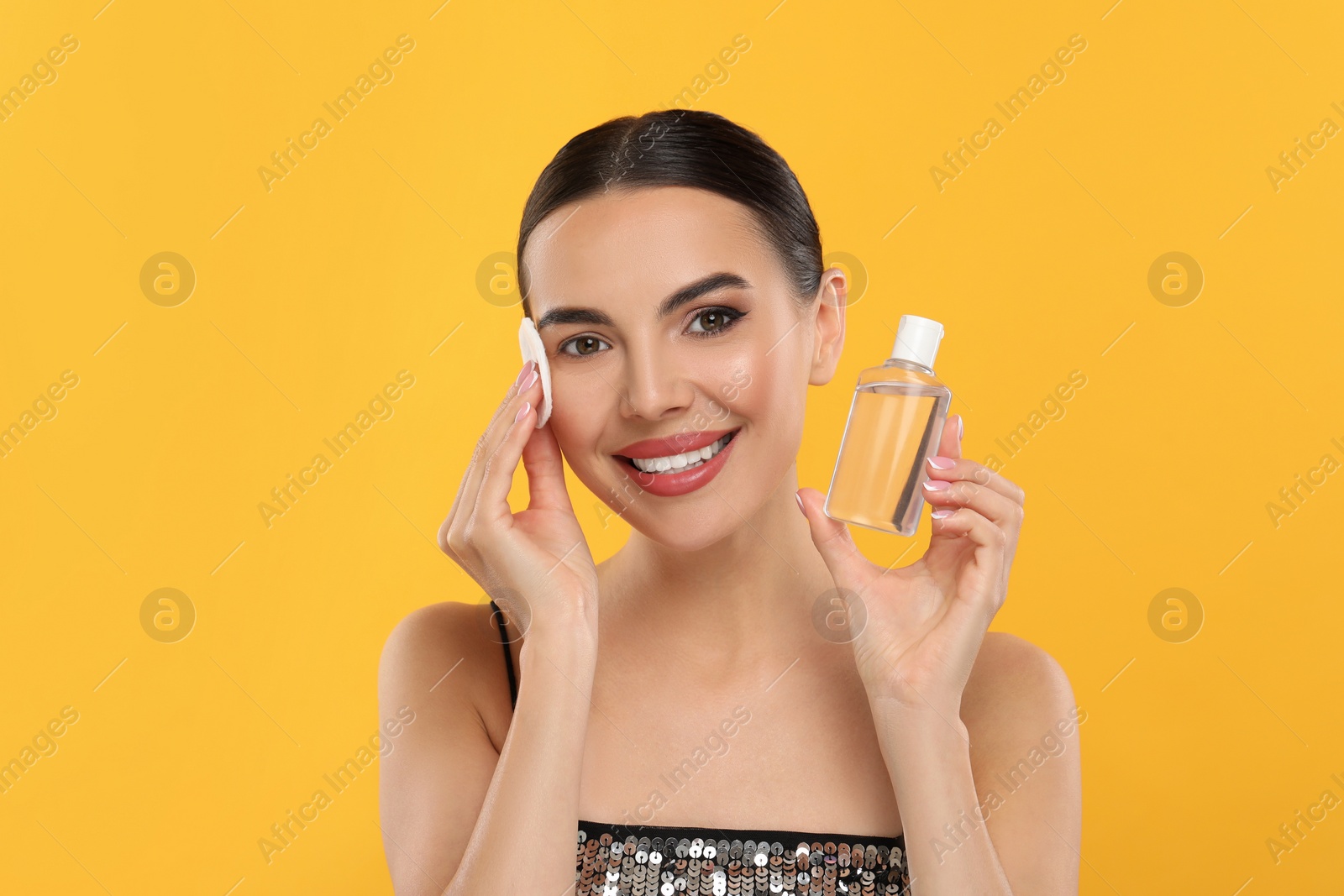 Photo of Beautiful woman removing makeup with cotton pad on orange background