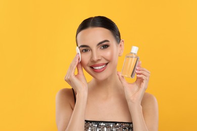 Photo of Beautiful woman removing makeup with cotton pad on orange background