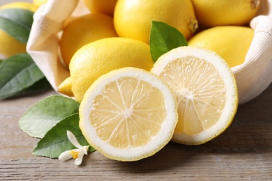 Many fresh ripe lemons with green leaves and flower on wooden table, closeup