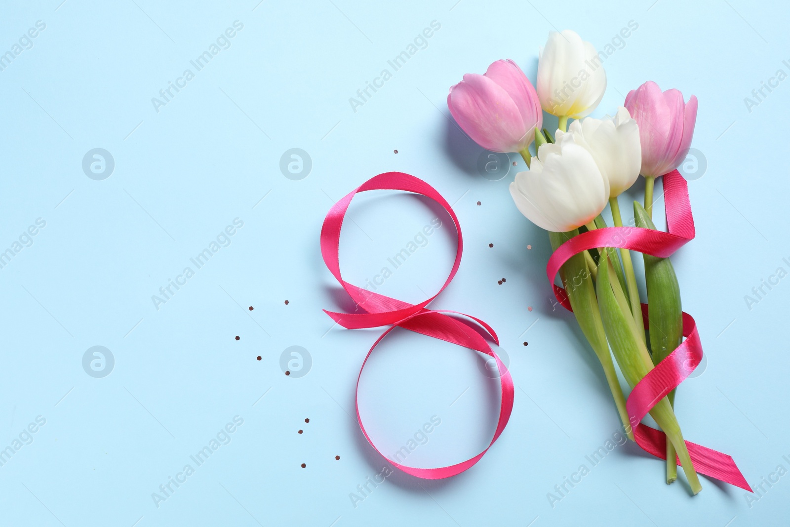 Photo of 8th of March greeting card design with pink ribbon, beautiful flowers and space for text on light blue background, flat lay. International Women's day