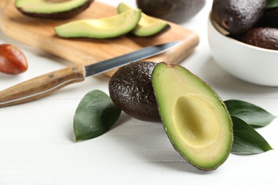 Whole and cut avocados with green leaves on white table