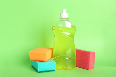 Photo of Bottle of detergent and sponges on green background