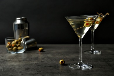 Photo of Glasses of Classic Dry Martini with olives on grey table against black background