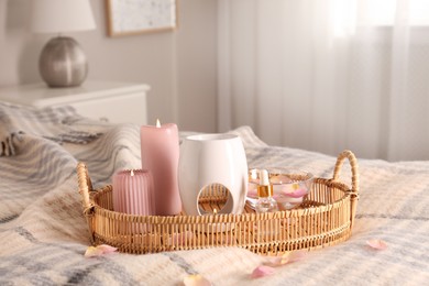 Photo of Aroma lamp, bottle of oil and burning candles on wicker tray in bedroom