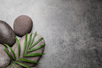 Photo of Spa stones and palm leaf on grey table, flat lay. Space for text