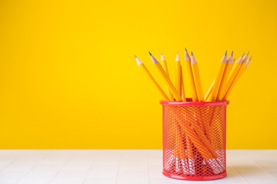 Photo of Many sharp pencils in holder on light table against yellow background, space for text