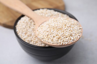 Photo of Dry barley groats in bowl and spoon on light grey table, closeup