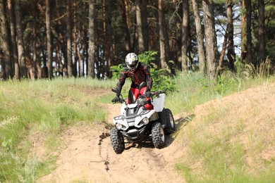 Photo of Man driving modern quad bike on sandy road near forest. Extreme sport