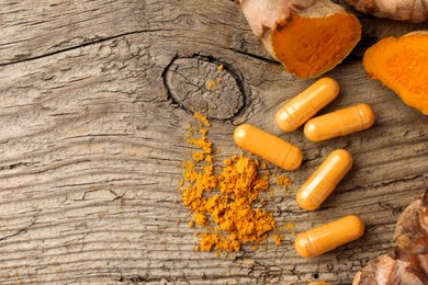 Photo of Aromatic turmeric powder, raw roots and pills on wooden surface, flat lay. Space for text