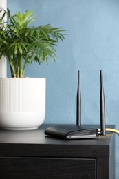 Modern Wi-Fi router near blue wall indoors