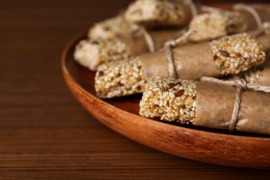 Plate with tasty sesame seed bars on wooden table, closeup