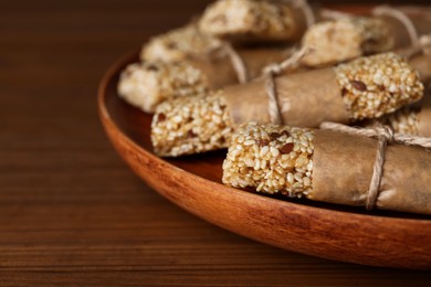 Photo of Plate with tasty sesame seed bars on wooden table, closeup