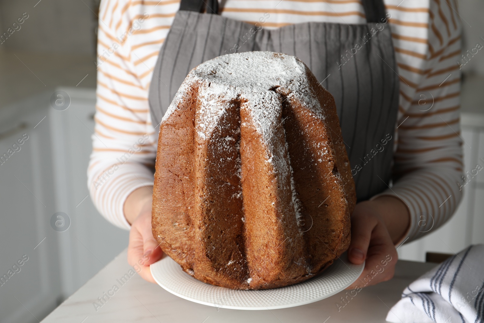 Photo of Woman holding delicious Pandoro cake decorated with powdered sugar in kitchen, closeup. Traditional Italian pastry