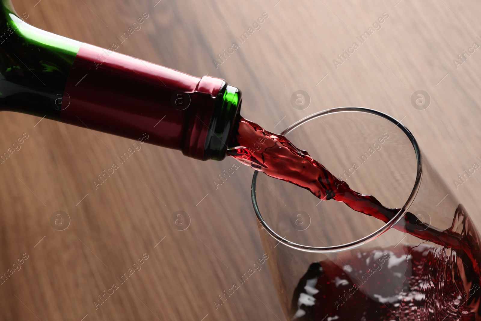 Photo of Pouring tasty red wine in glass at wooden table, closeup