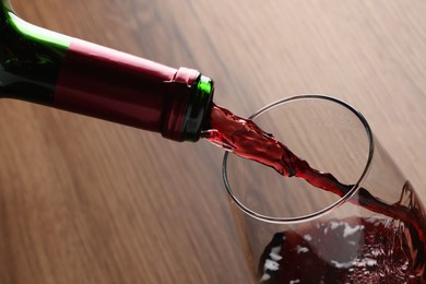 Pouring tasty red wine in glass at wooden table, closeup