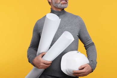 Photo of Architect with hard hat and drafts on orange background, closeup