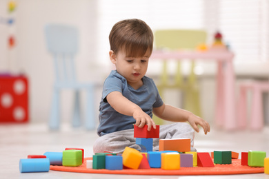 Photo of Cute little child playing with toy blocks on floor at home