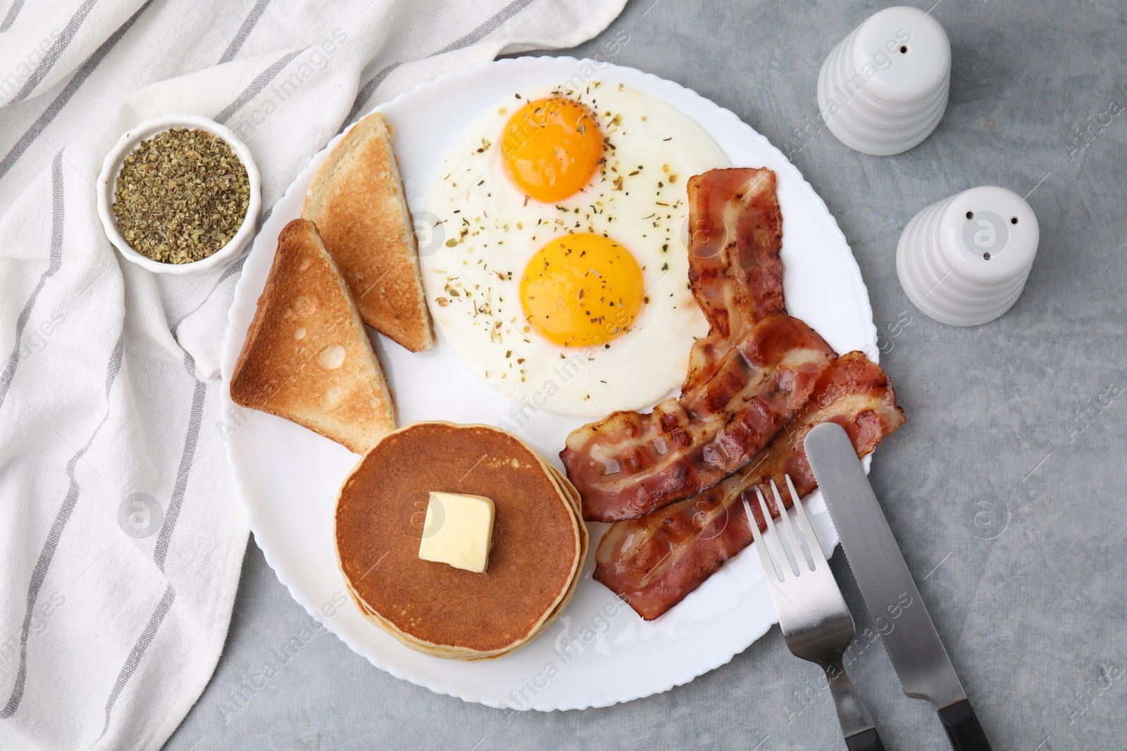 Photo of Tasty pancakes served with fried eggs and bacon on grey table, flat lay