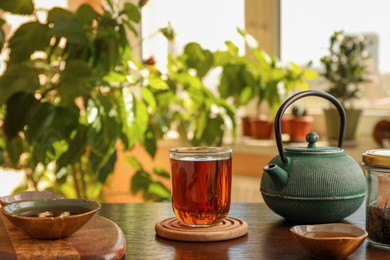 Photo of Teapot and cups of freshly brewed tea on wooden table indoors. Traditional ceremony