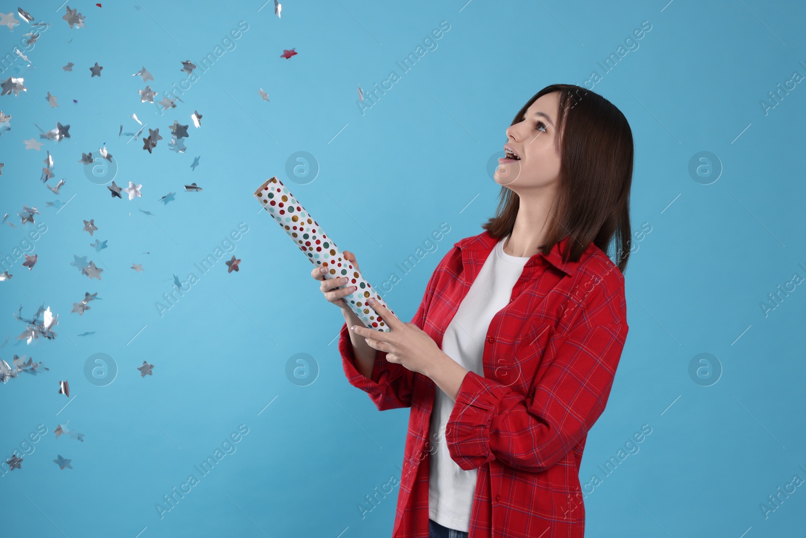 Photo of Happy teenage girl blowing up party popper on light blue background