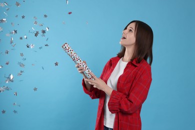 Photo of Happy teenage girl blowing up party popper on light blue background