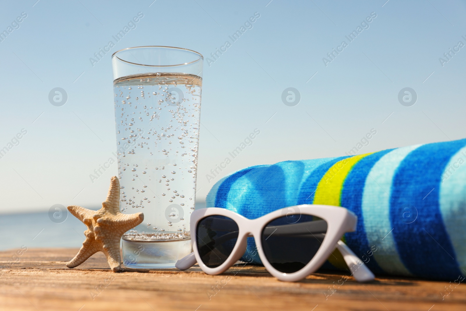 Photo of Wooden deck with glass of refreshing drink and beach accessories on hot summer day