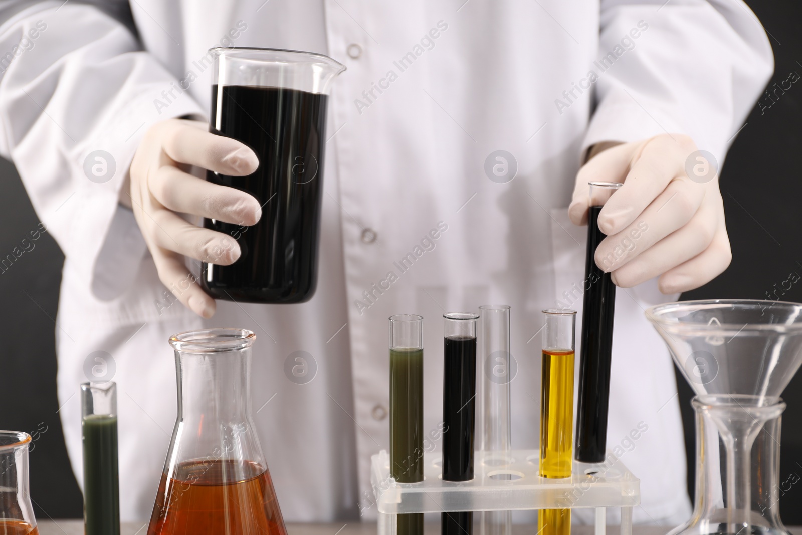 Photo of Woman holding beaker and test tube with black crude oil on dark background, closeup