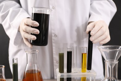 Woman holding beaker and test tube with black crude oil on dark background, closeup