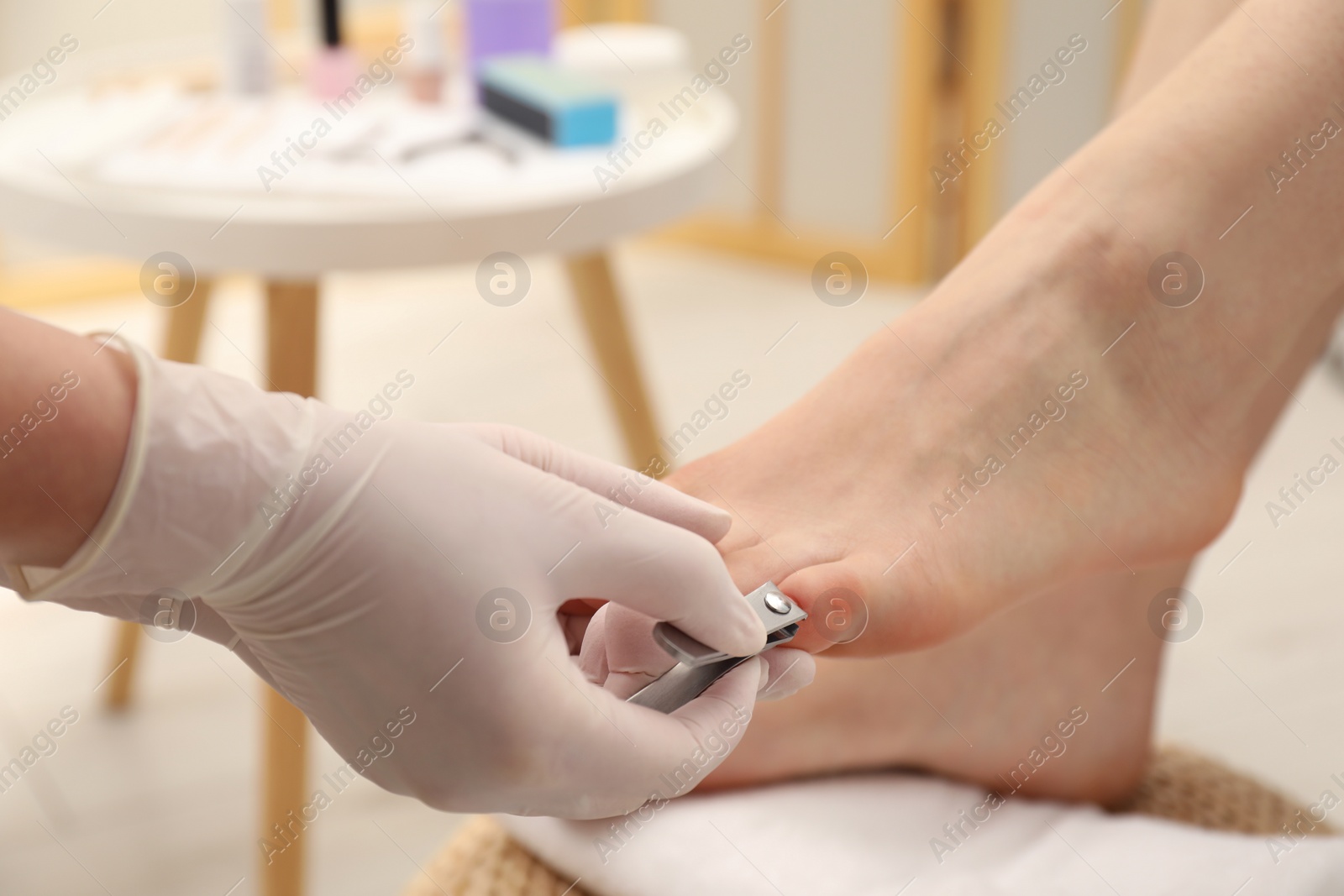 Photo of Professional pedicurist cutting client`s toenails with clipper in beauty salon, closeup