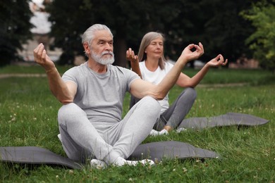 Photo of Senior couple practicing yoga on green grass in park, selective focus