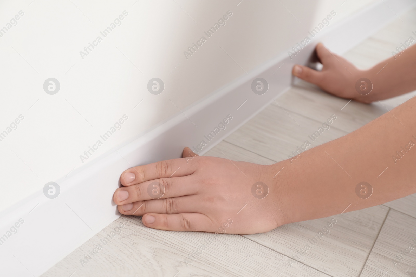 Photo of Man installing plinth on laminated floor in room, closeup