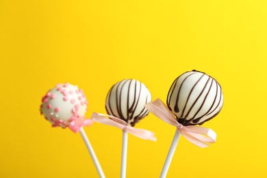 Tasty cake pops with bows on yellow background