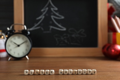 Photo of Cubes with phrase Winter Holidays on wooden table in classroom. Space for text