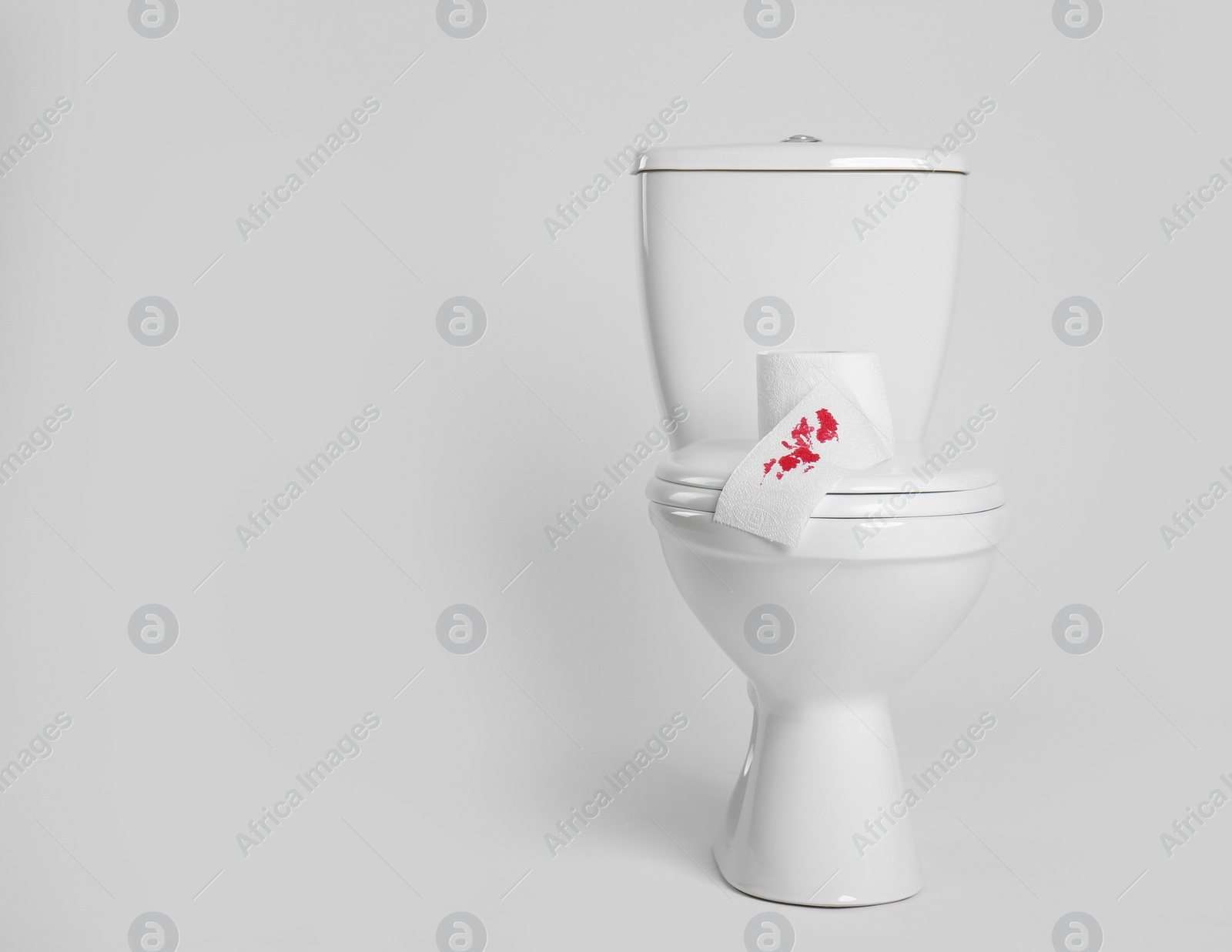 Photo of Paper with blood stain on toilet bowl against white background. Hemorrhoids concept