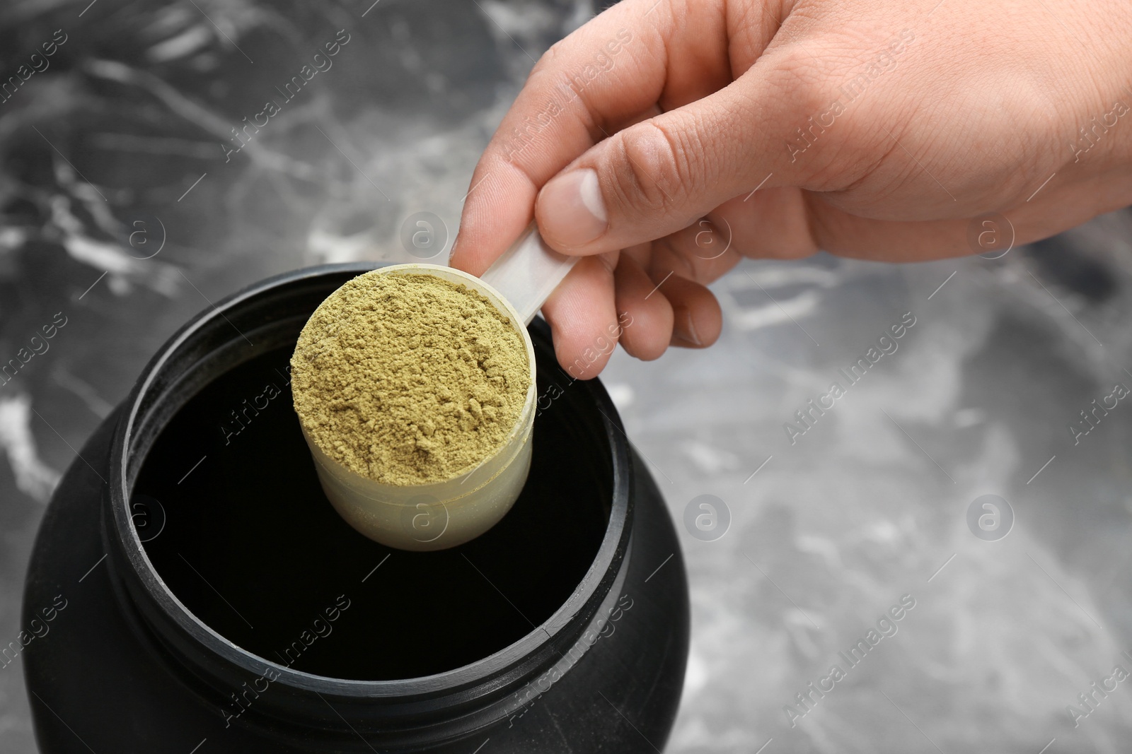 Photo of Man holding measuring spoon with hemp protein powder over jar on table