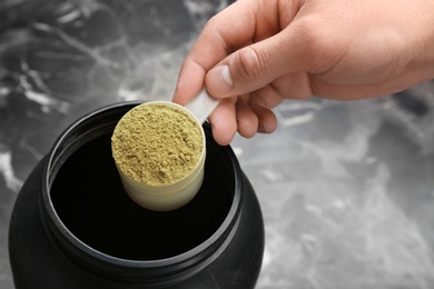 Man holding measuring spoon with hemp protein powder over jar on table