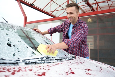 Young man cleaning vehicle with sponge at self-service car wash