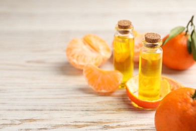 Photo of Bottles of tangerine essential oil, fresh fruits and peel on white wooden table. Space for text