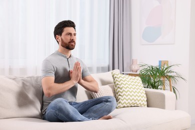Man meditating on sofa at home, space for text