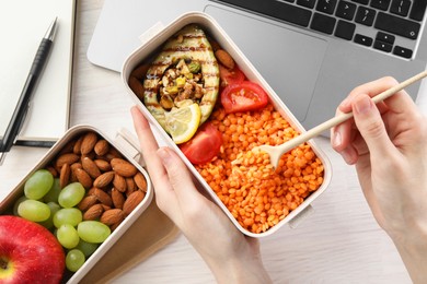 Photo of Woman eating healthy products high in vegetable fats near laptop at light wooden table, top view