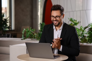 Photo of Happy young man with laptop at table in office