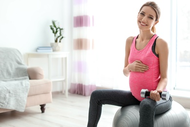 Photo of Young pregnant woman doing exercises with dumbbell at home