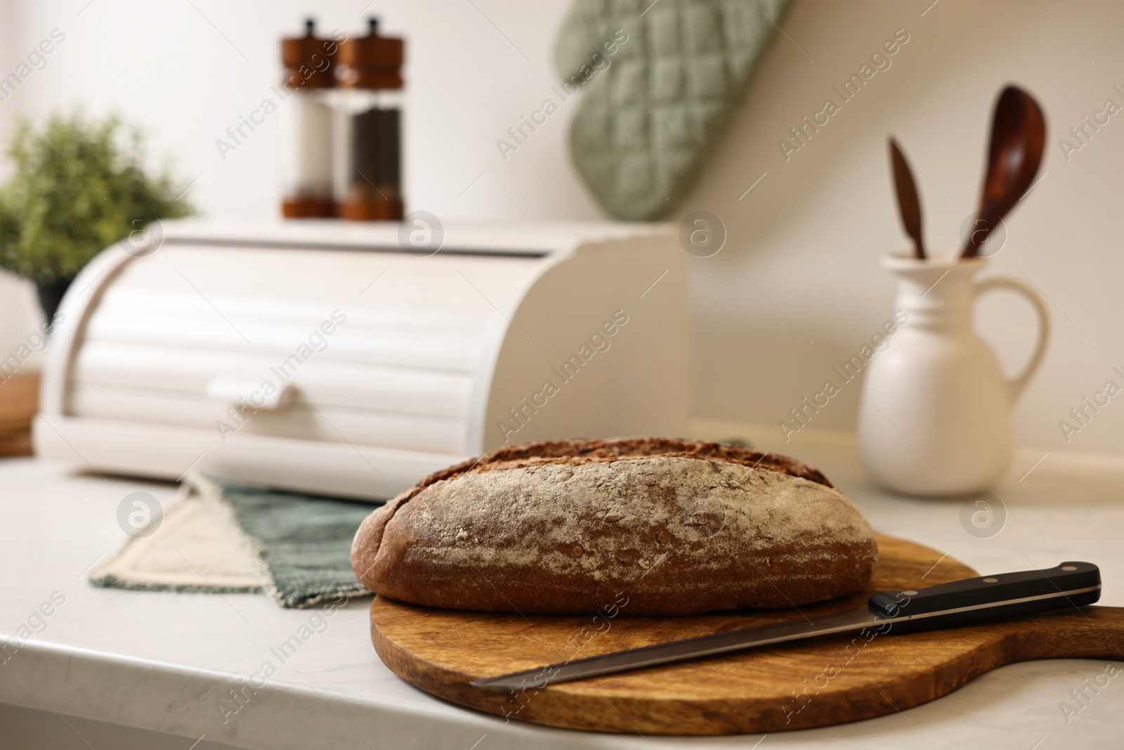 Photo of Wooden bread basket and freshly baked loaf on white marble table in kitchen